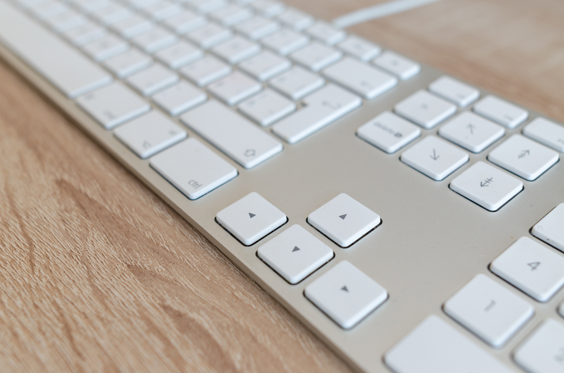 Nahaufnahme einer weissen Aluminium-Tastatur auf hellem Holzschreibtisch